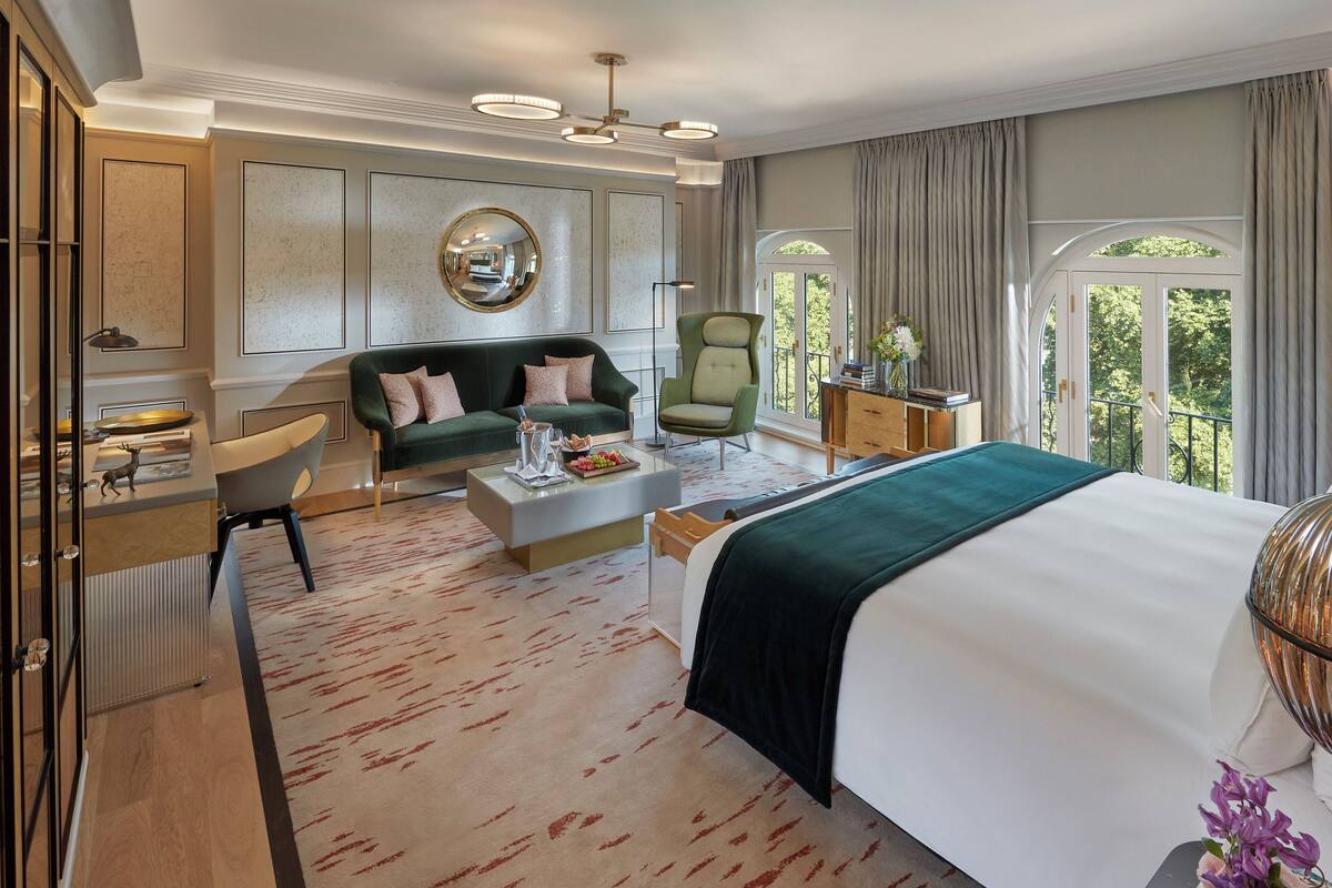 Ein modernes Hotelzimmer mit einem großen Bett, einer grünen Couch, einem Schreibtisch und einem Stuhl. Es gibt ein großes Fenster mit Vorhängen, einen Spiegel an der Wand und eine dekorative Vase auf dem Schreibtisch.