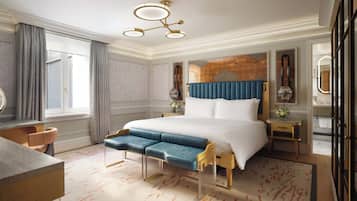A hotel room with a large bed, a desk, a chair, a vanity with a mirror, and a window with curtains.