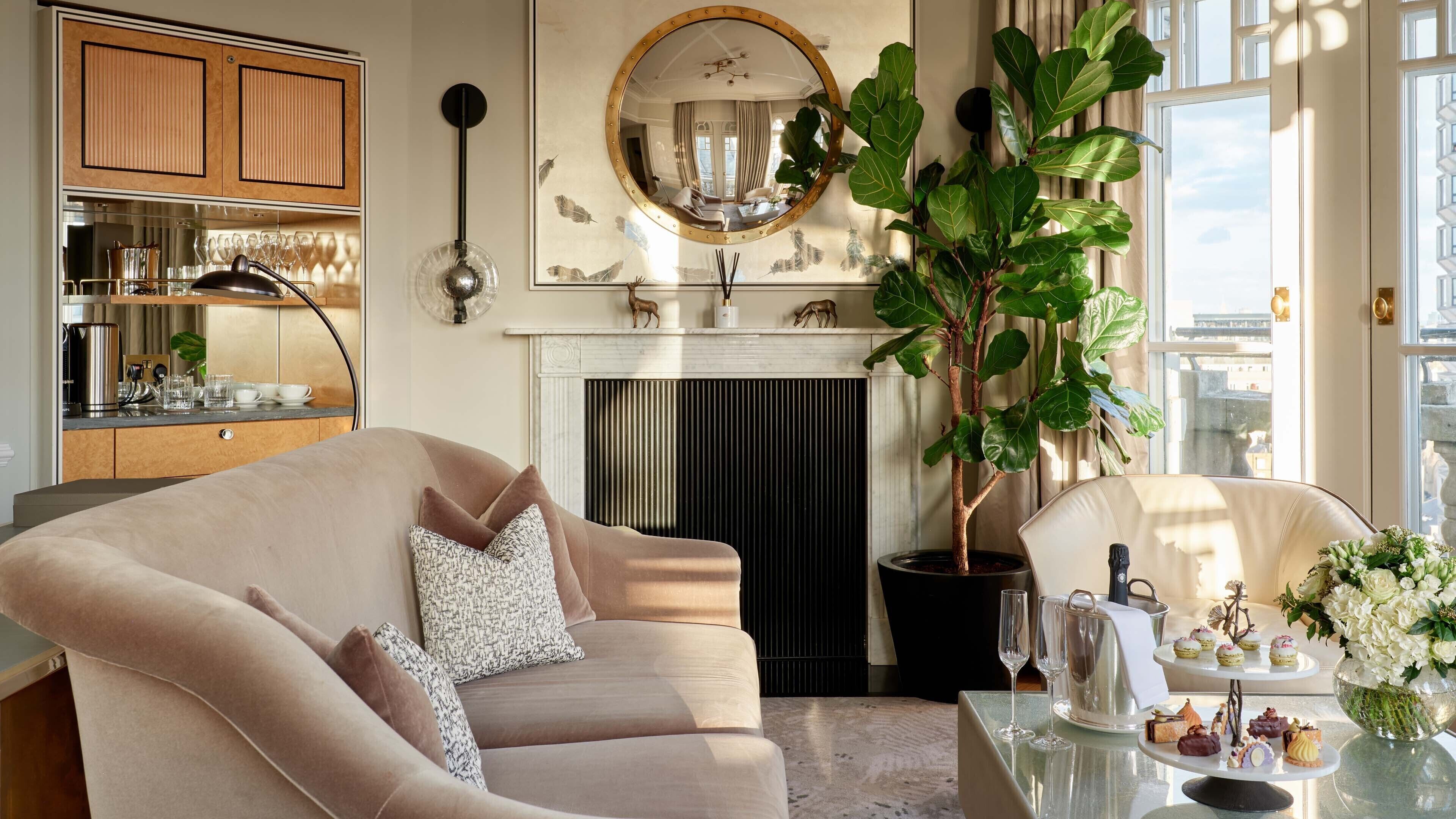 Ein Wohnzimmer mit einem beigefarbenen Sofa, einem Kamin, einem großen Spiegel und einem Esstisch mit einer Blumenkomposition.