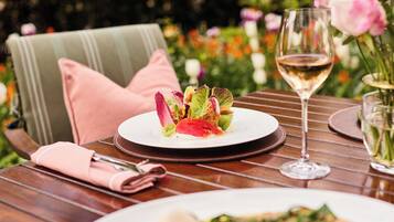 A dining table with a plate of food, a glass of wine, and a vase of flowers.