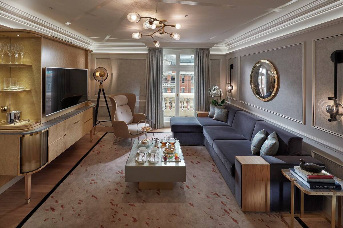 Una sala de estar moderna con un sofá, una mesa de centro y un televisor. Hay un ventanal con cortinas, un candelabro y un espejo en la pared.