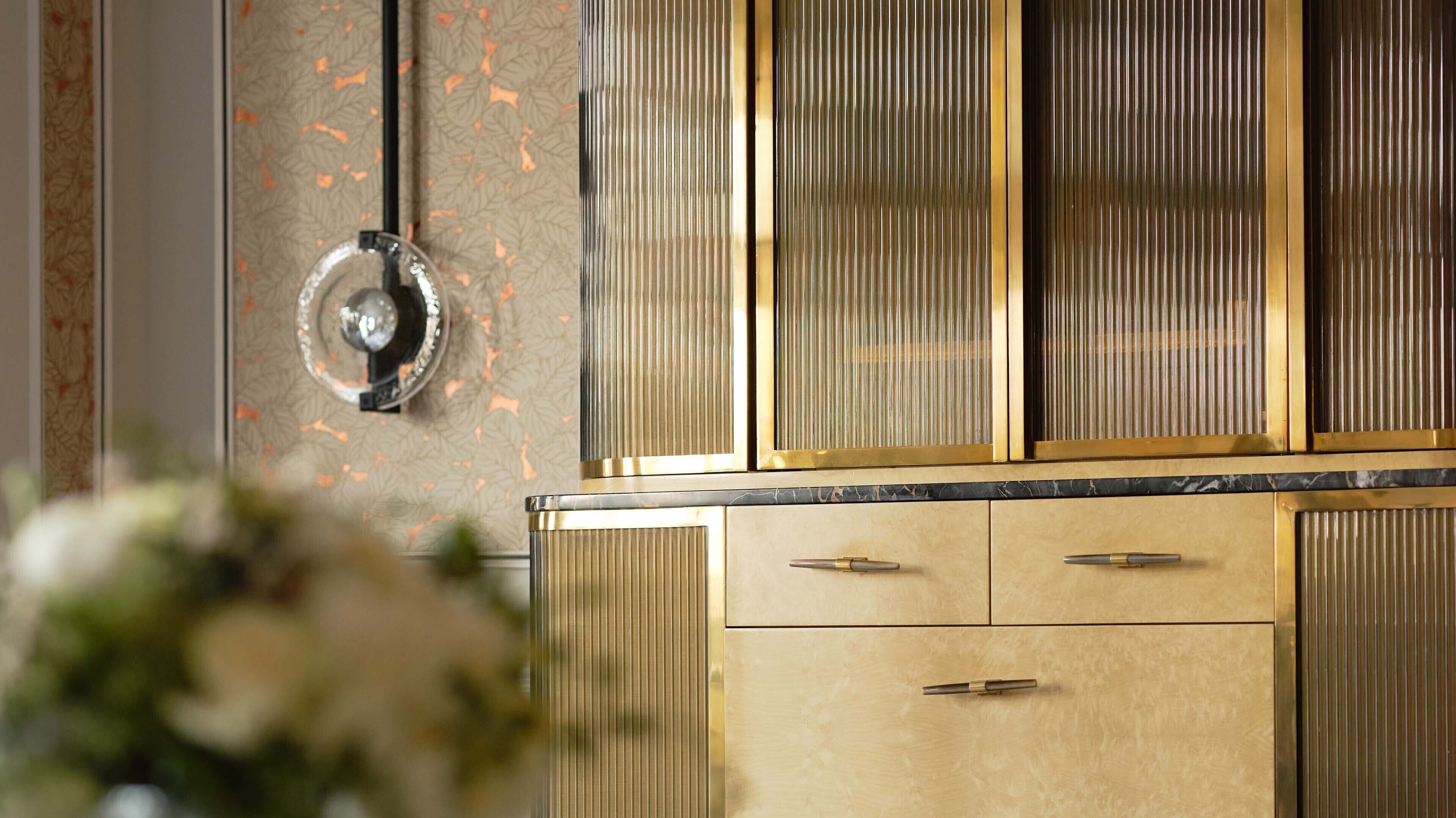 A kitchen with a marble countertop, gold-toned cabinets, and a central round metallic fixture.
