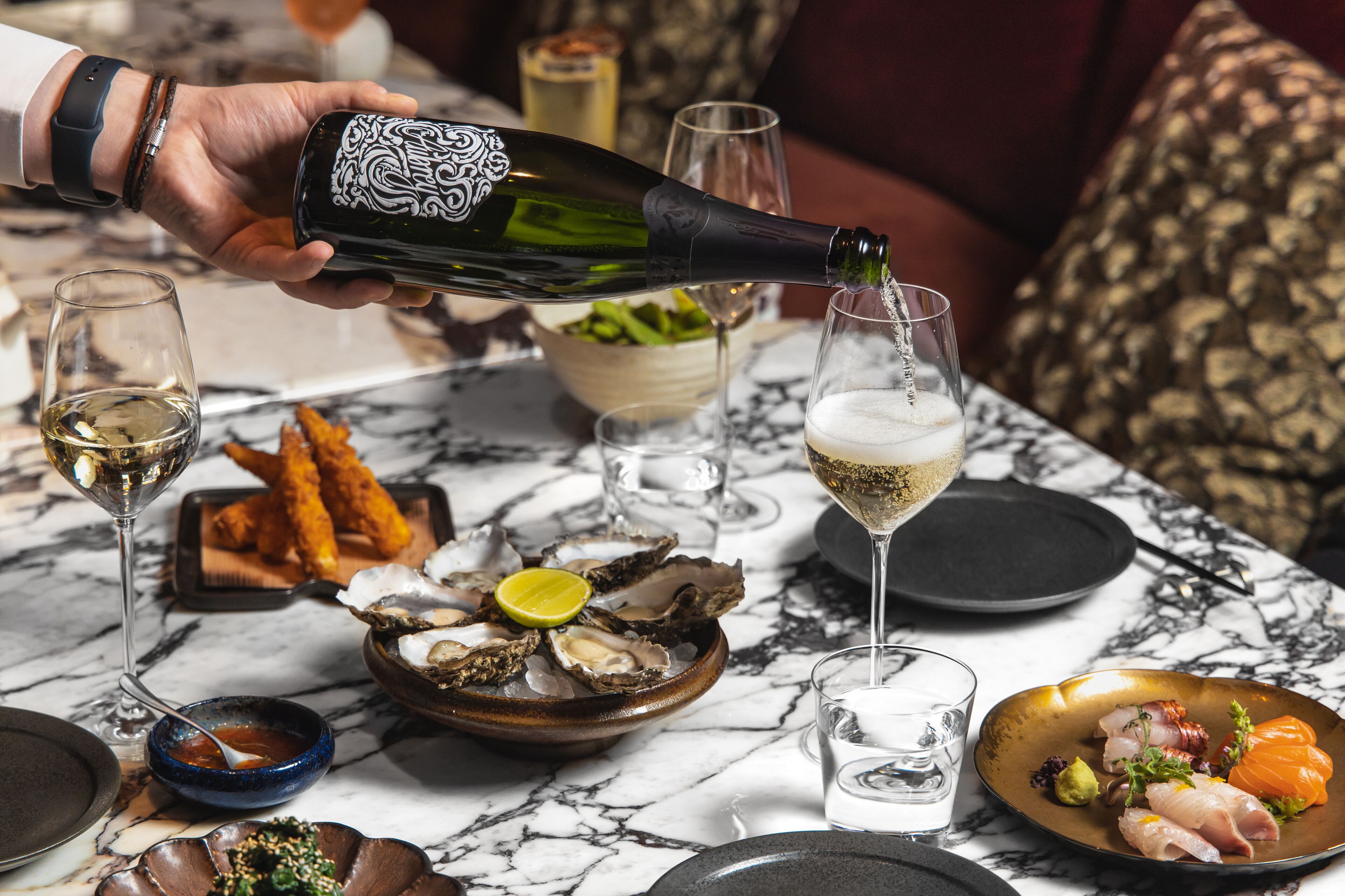 A dining table with a variety of seafood dishes, a bottle of champagne being poured, and several glasses.