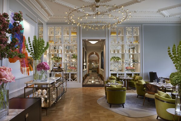 Een ruime hotel lobby met een centraal hanglamp, een lange receptiebalie en zicht op de eetruimte.