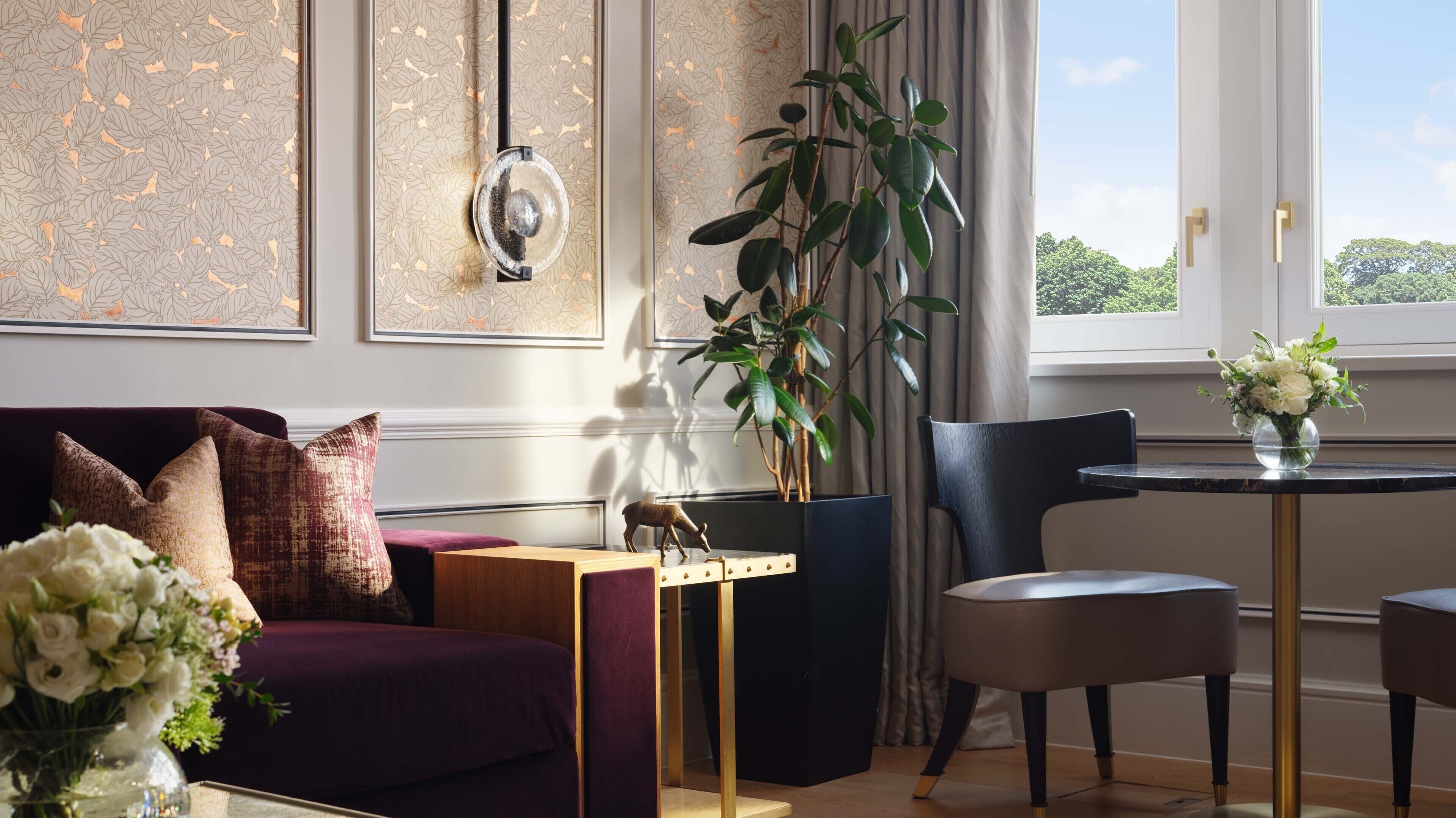 A modern living room with a purple sofa, a wooden coffee table, a black chair, and a small round table with a vase of flowers.