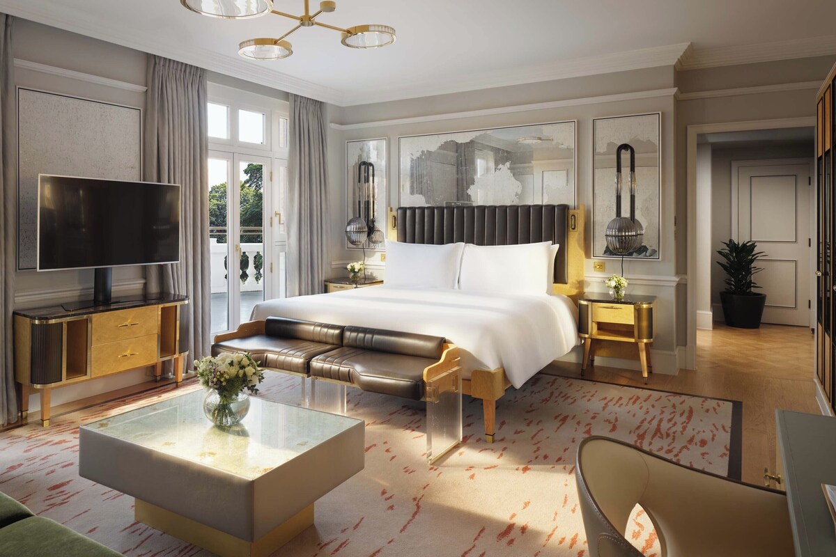 A modern hotel room with a large bed, a flat-screen TV, a sofa, a coffee table, and a potted plant.