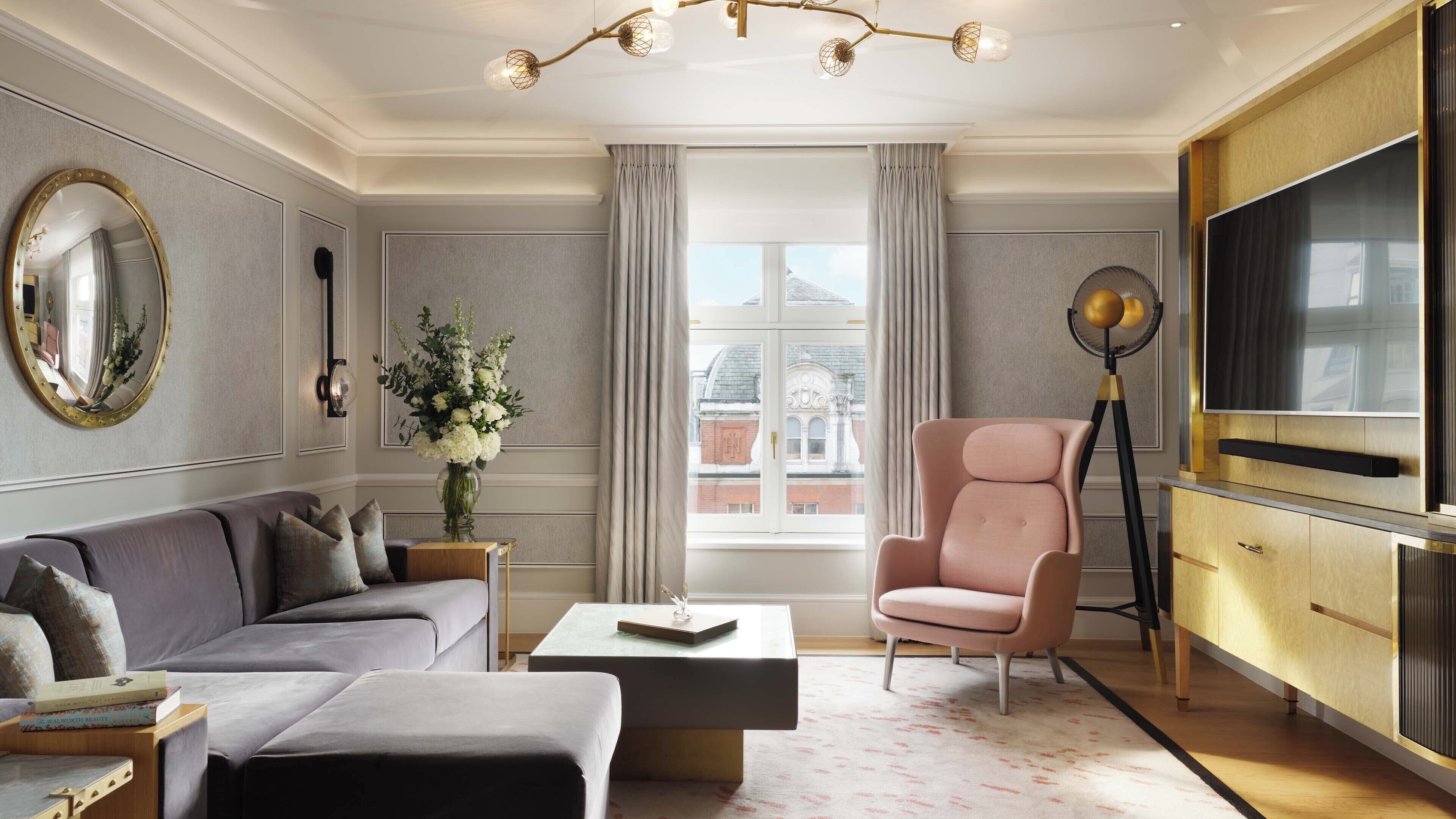 A modern living room with a grey sofa, a pink armchair, a coffee table, and a large flat-screen TV.
