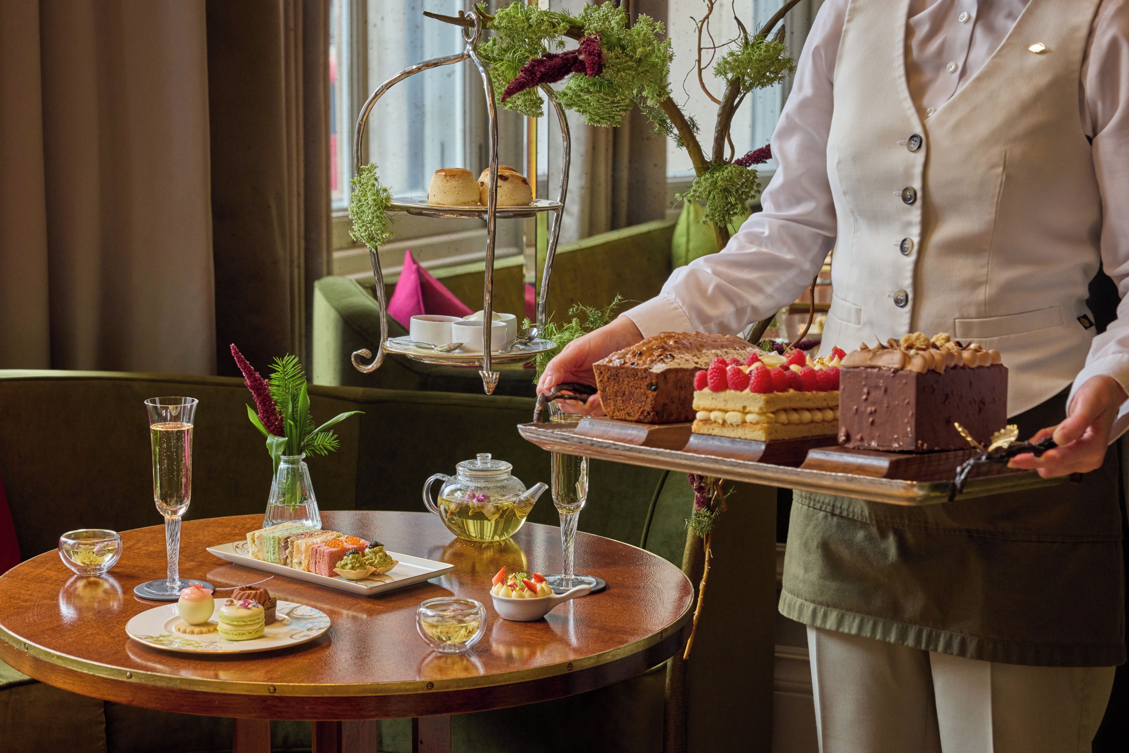 A table with a tiered dessert stand, a teapot, and various small dishes of food and drinks.