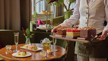 A table with a tiered dessert stand, a teapot, and various small dishes of food and drinks.