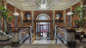 A grand lobby with marble columns, a grand chandelier, and a staircase leading to an entrance.