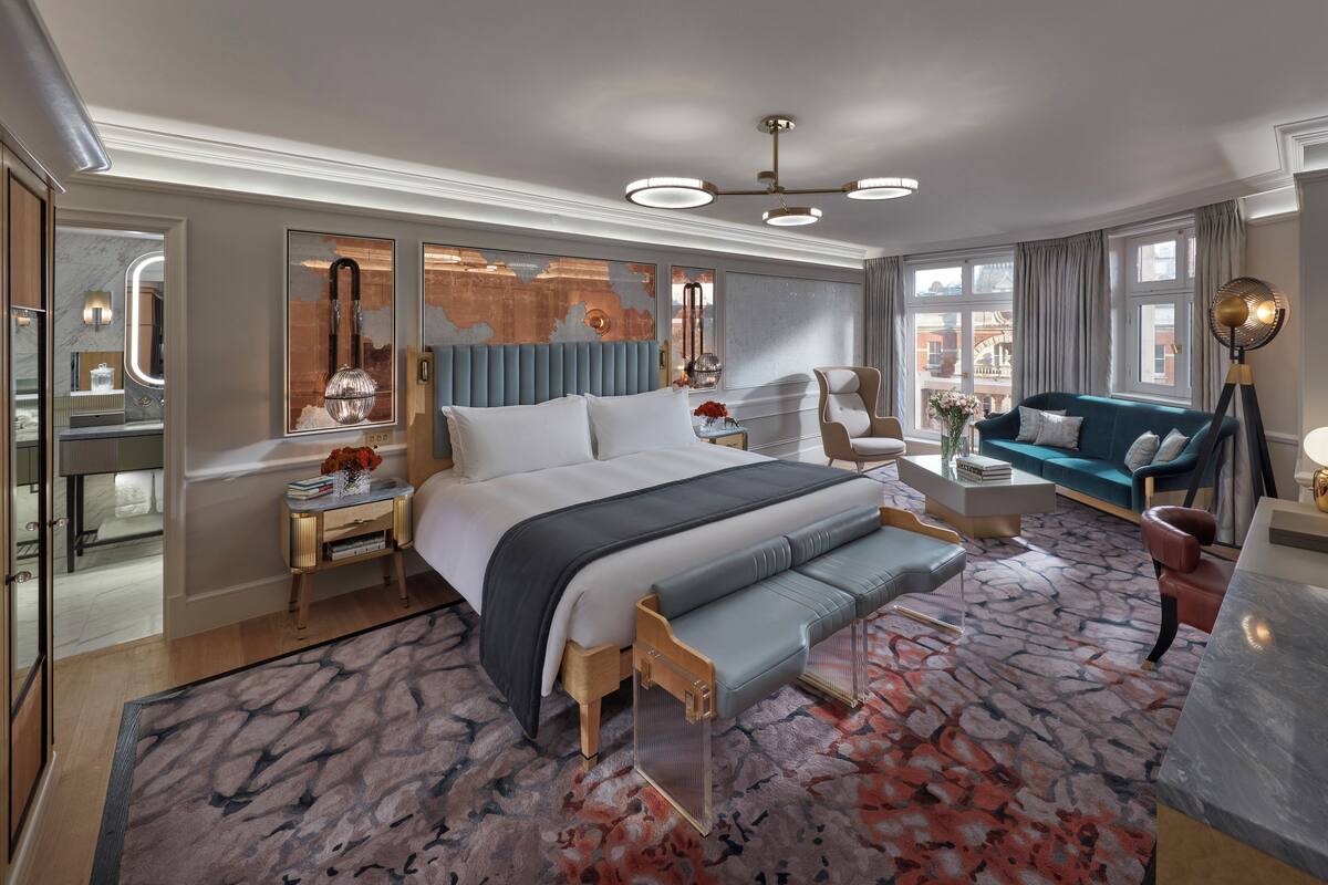 Ein modernes Hotelzimmer mit einem großen Bett, einer Sitzecke, einem Schminktisch und Blick auf die Stadt.