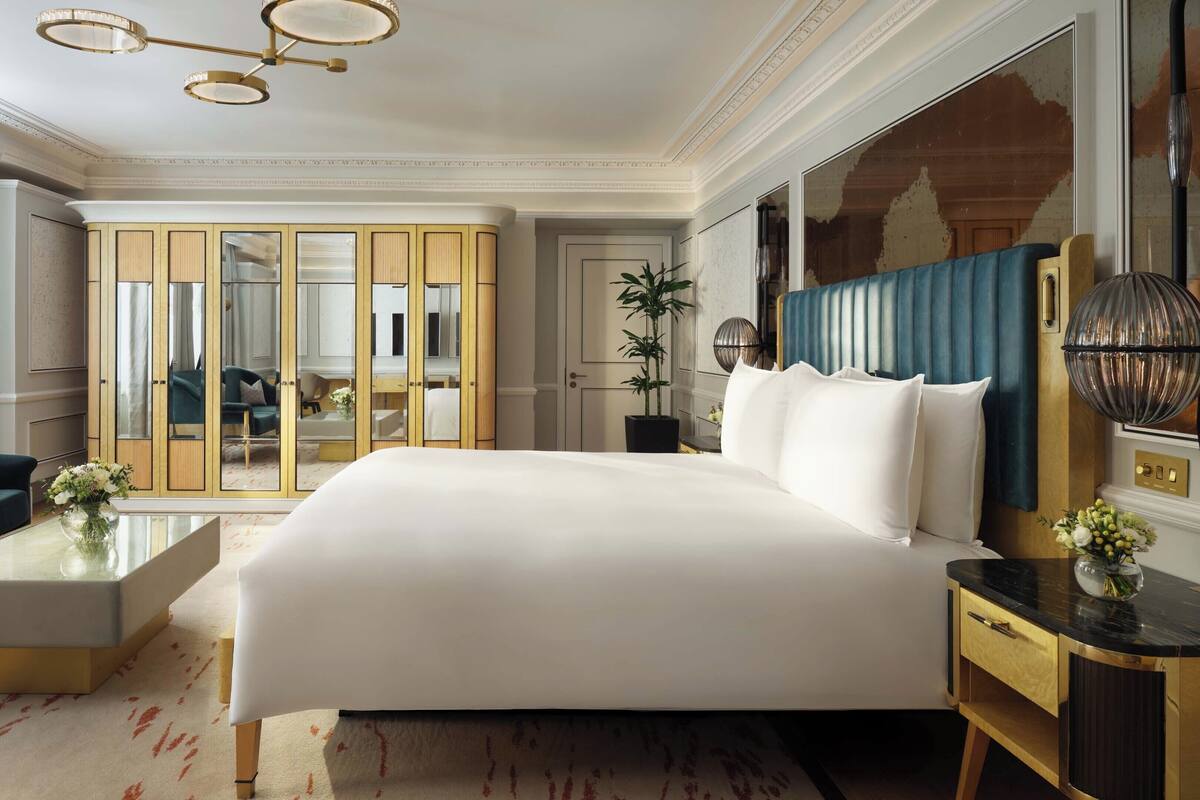 Ein geräumiges Schlafzimmer mit einem großen Bett, einem Schlafsofa, einem Nachttisch und einem Spiegel. Es gibt einen Kleiderschrank mit Spiegel, eine Zimmerpflanze und eine Chandelier.