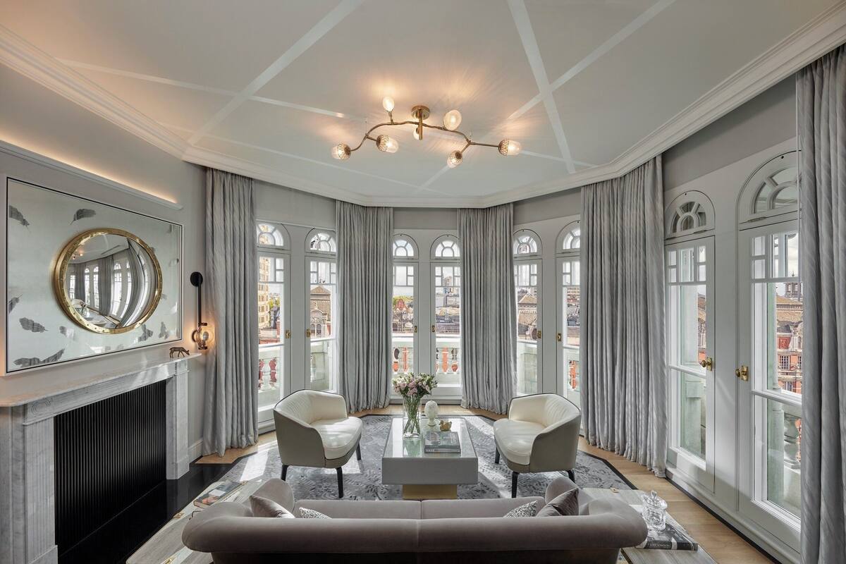 Ein luxuriöses Wohnzimmer mit Kamin, zwei Sesseln, einer Couch und einer Kristallleuchtre.'