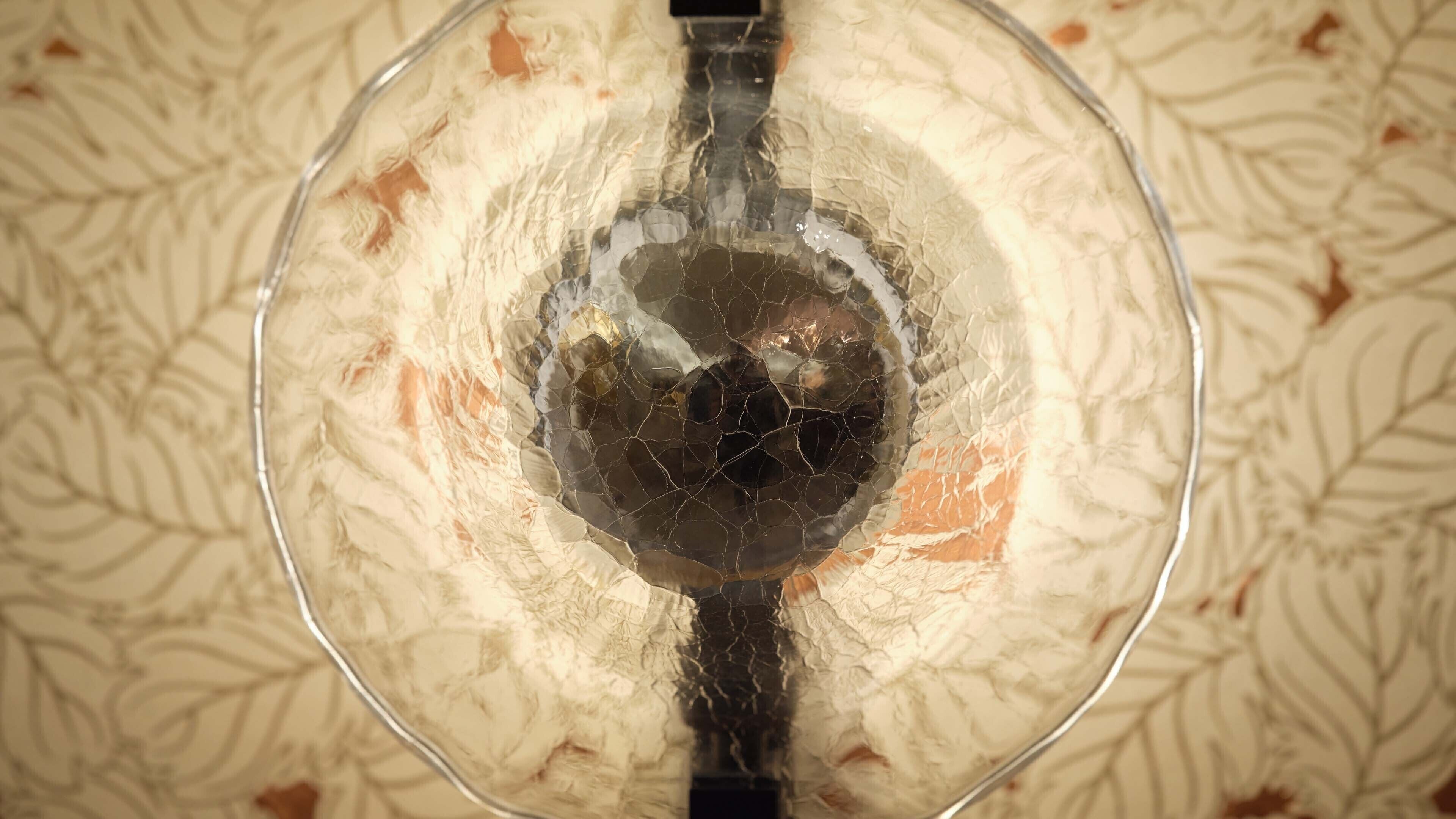 Eine transparente Glaskugel mit einem schwarzen Gegenstand darin, auf einer gemusterten Oberfläche platziert.