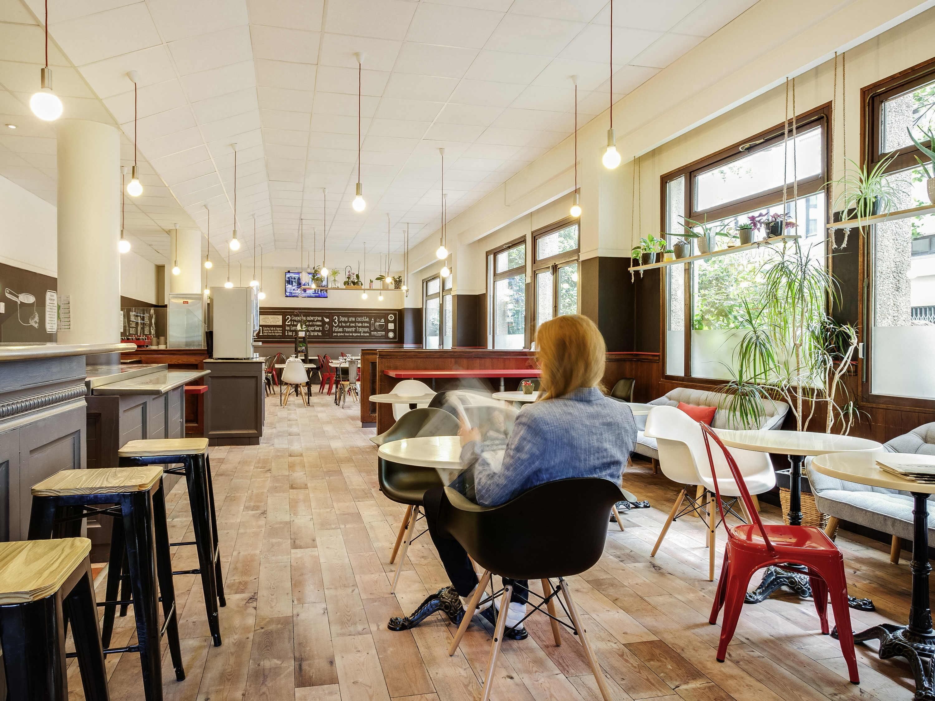 A spacious cafe with wooden flooring, multiple seating areas, and large windows allowing natural light.