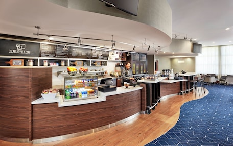 A modern bistro with a curved counter, a variety of food and drink options, and a seating area with tables and chairs.