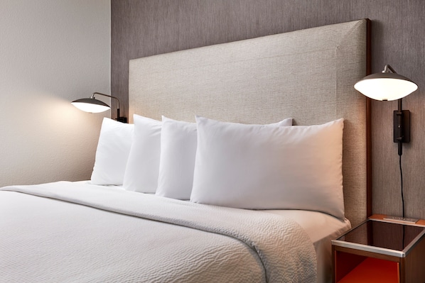 A neatly made bed with white linens and pillows, a headboard, and two bedside lamps.