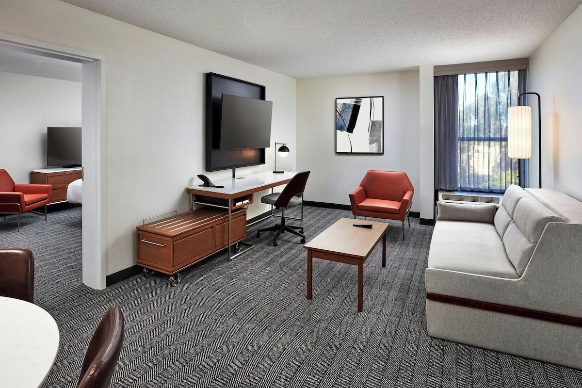 A hotel room with a flat-screen TV, a desk with a chair, a sofa, and a dining area with chairs.