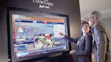 A digital display at a Courtyard Marriott hotel, featuring a GoBoard interface with local weather, news, and market information.