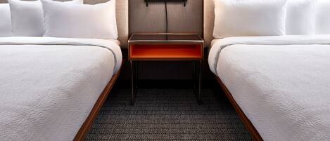 A hotel room with two beds, a nightstand with a lamp, and a carpeted floor.