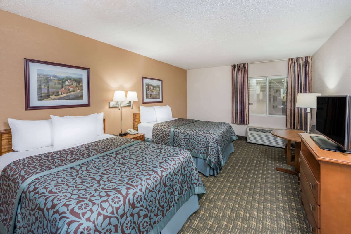 A hotel room with two beds, a TV, a desk, and a window with curtains.