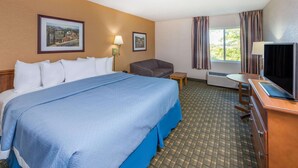 A hotel room with a large bed, a desk with a TV, a chair, a small table, and two wall-mounted lamps. - Days Inn by Wyndham Kirksville (Kirksville)
