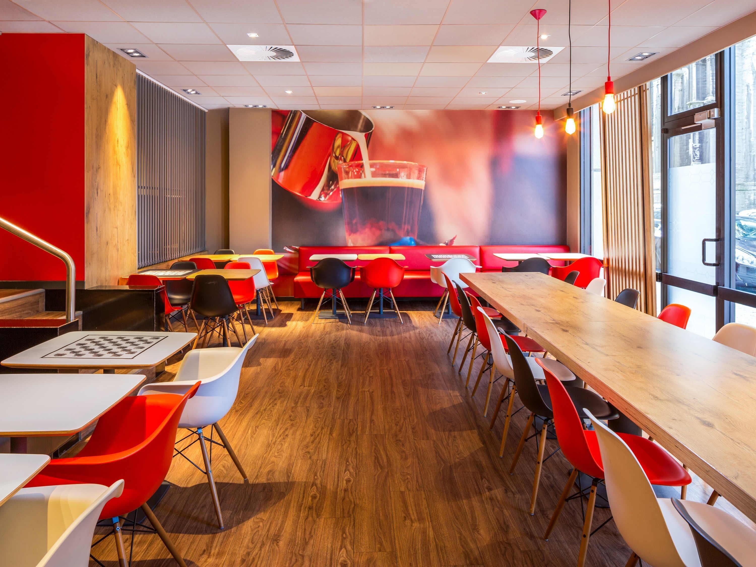 A modern restaurant with red and white seating, wooden tables, and a large mural on the back wall.