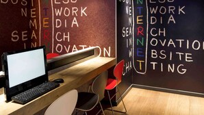 Un espacio de trabajo con una computadora, un escritorio y una silla. La pared de fondo muestra palabras relacionadas con negocios e innovación.