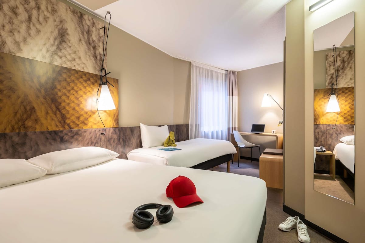 A hotel room with two beds, a desk, a chair, a laptop, a telephone, and a mirror.