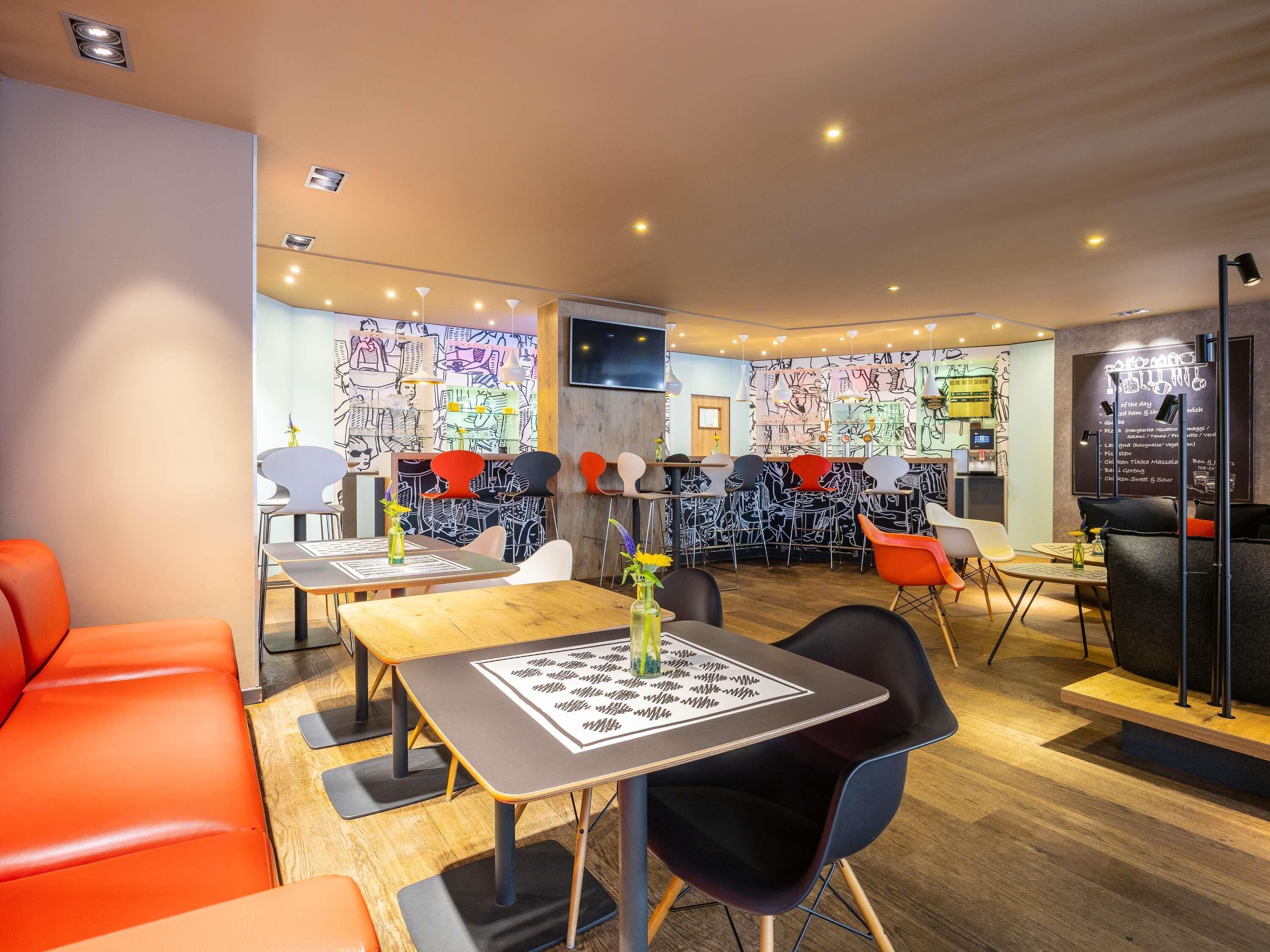 Restaurante moderno com área de bar, mesas e cadeiras, e um quadro de cardápio.