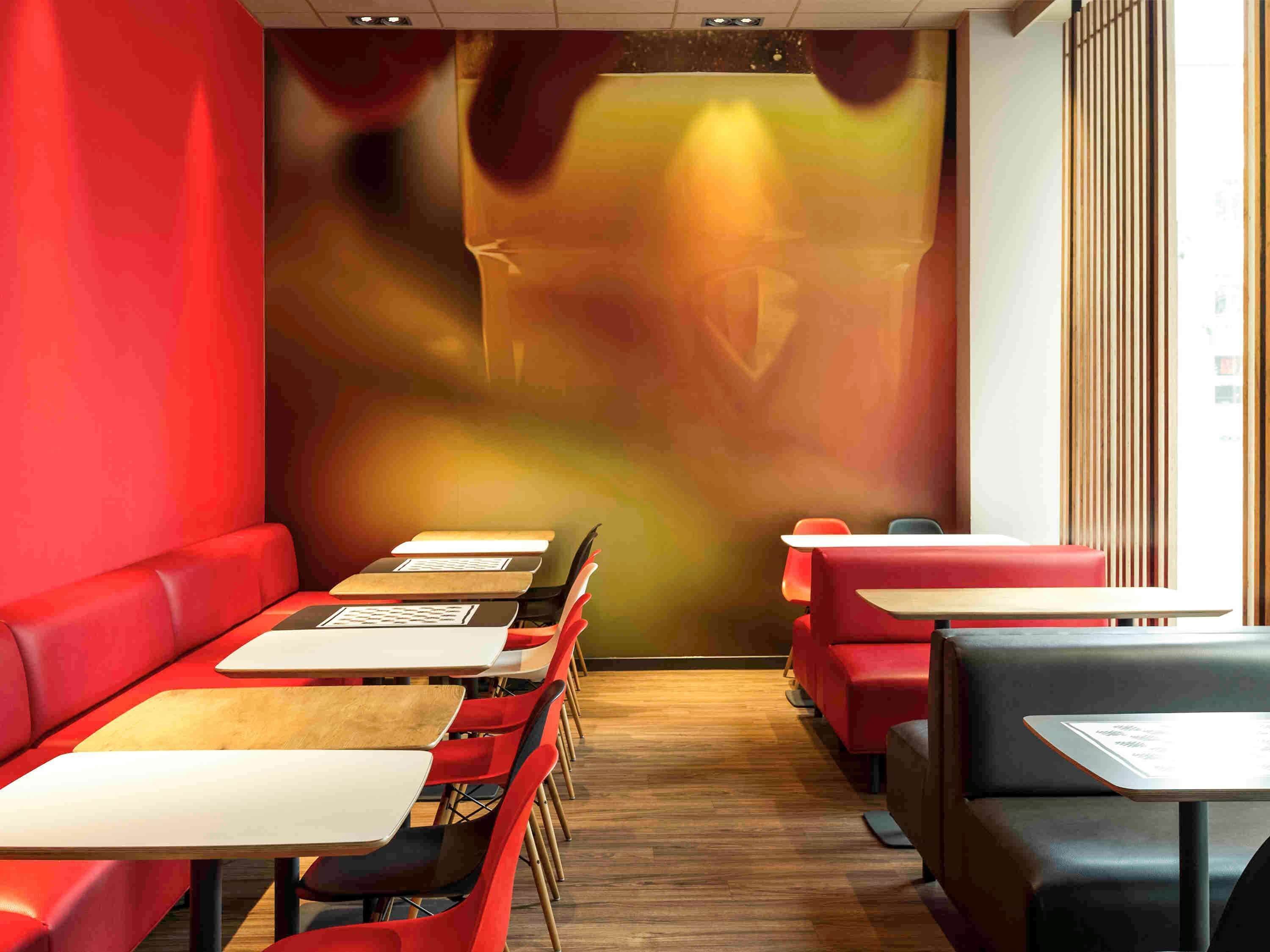 A restaurant interior with red seating, wooden tables, and a large abstract mural on the wall.