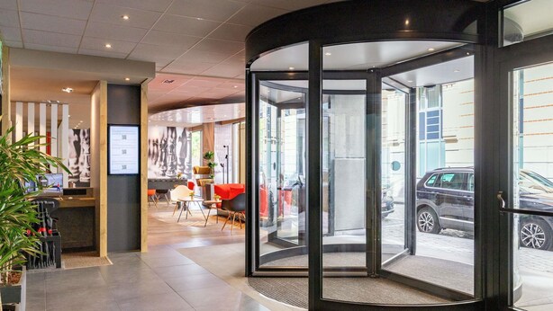 Vestíbulo de hotel con puerta giratoria, zona de estar y mostrador de recepción.