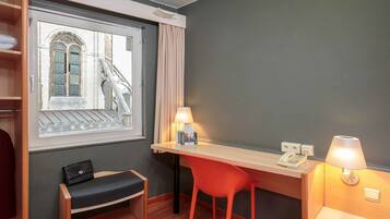 Habitación de hotel con escritorio, dos sillas, un banco, una ventana que ofrece vistas a un puente y una lámpara.