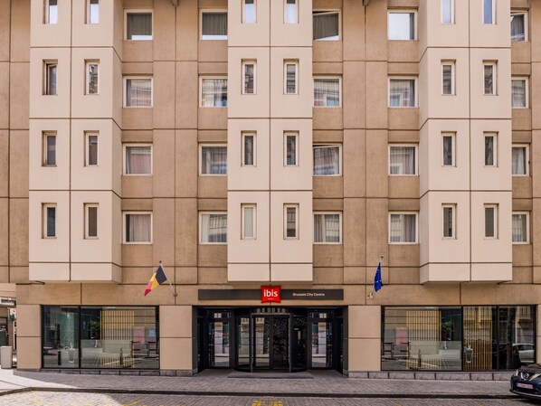 A multi-story hotel with a central entrance, a red sign, and two flags.