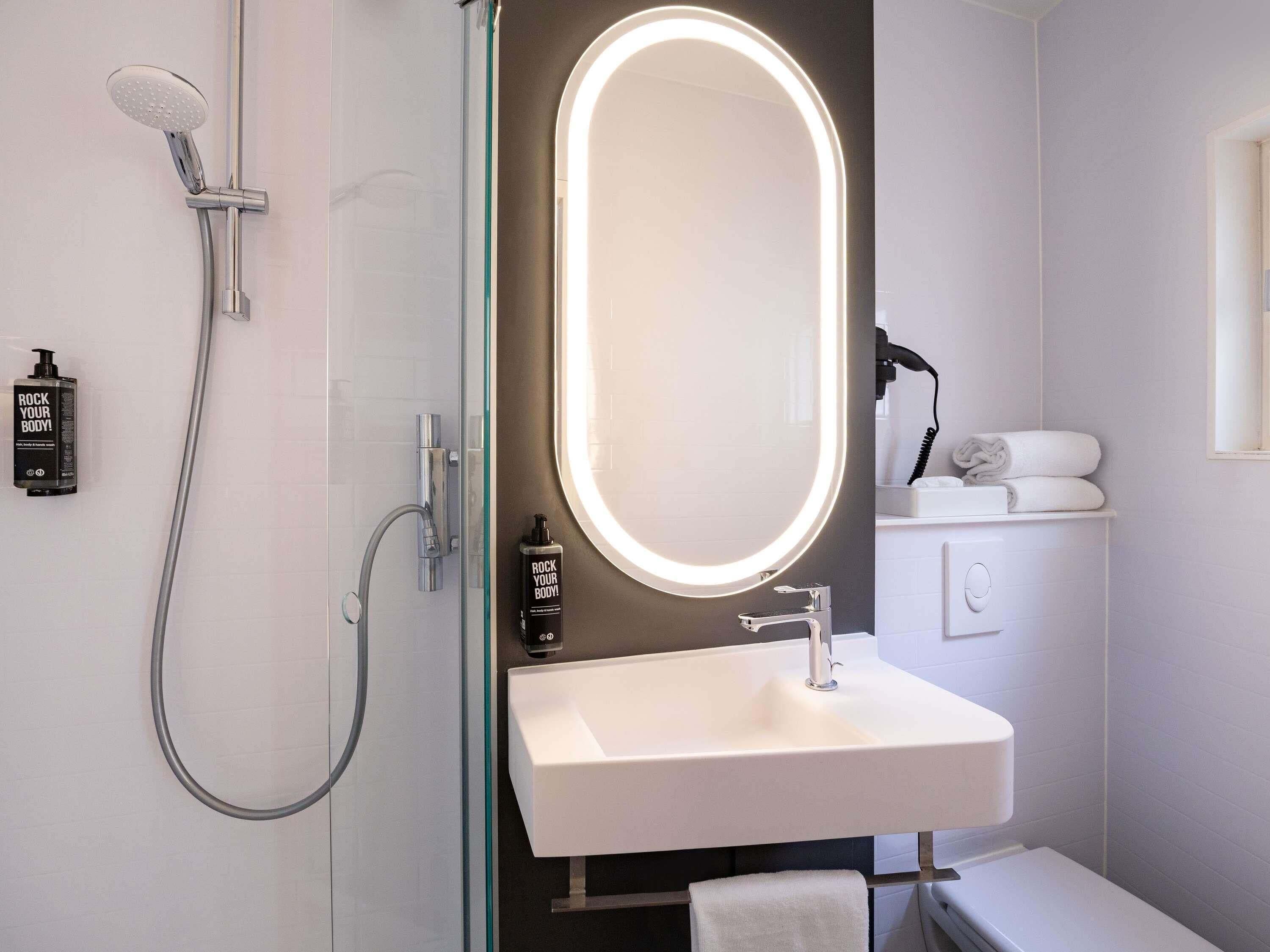 Un baño moderno con ducha de vidrio, lavamanos blanco y espejo con marco iluminado.
