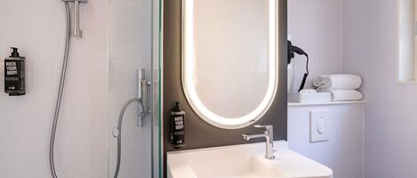 A modern bathroom with a glass-enclosed shower, a white sink, and a mirror with a lighted frame.