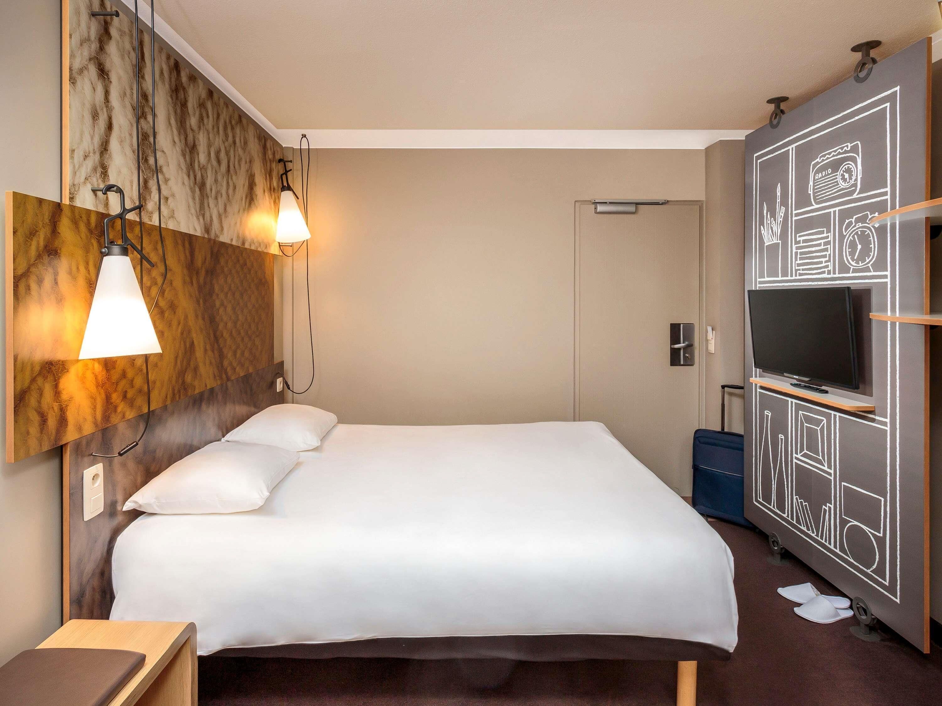 Una habitación de hotel con cama, lámparas de noche, televisor y una pared con diseño de pizarra.