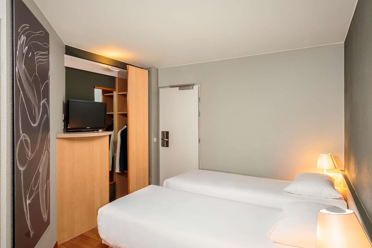 A hotel room with a bed, bedside lamp, TV, wardrobe, and a door.