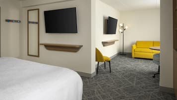 A hotel room with a large bed, a flat-screen TV mounted on the wall, a small desk with a chair, and a yellow sofa.