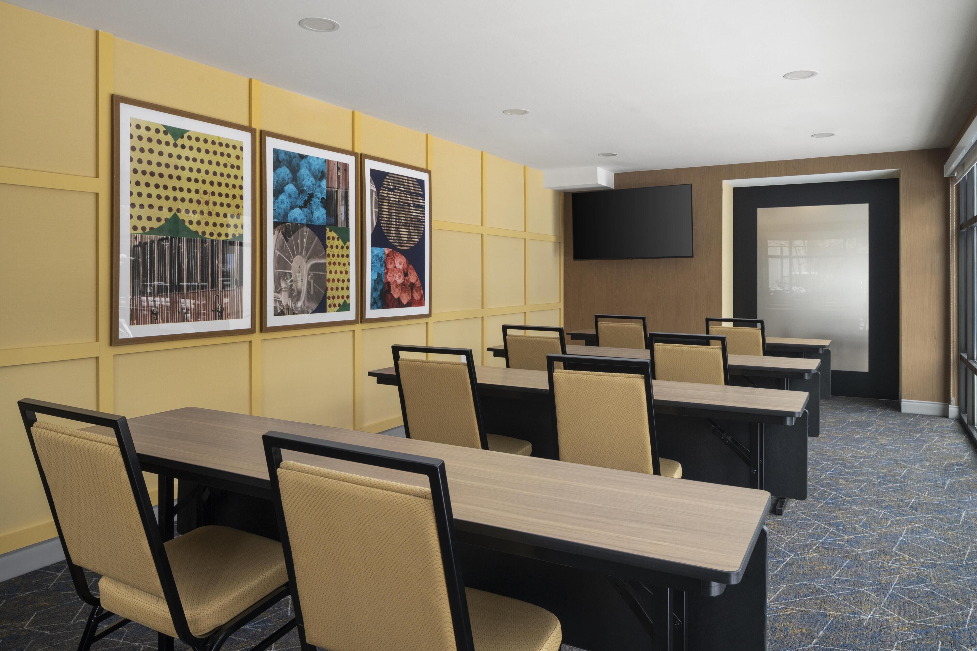 A conference room with multiple tables and chairs, framed artwork on the walls, and a flat-screen TV.