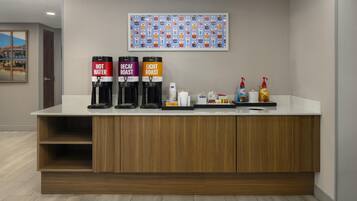 Zona de recepción de hotel con mostrador, máquinas de café de agua caliente, descafeinado y tueste claro, y artículos de aseo.