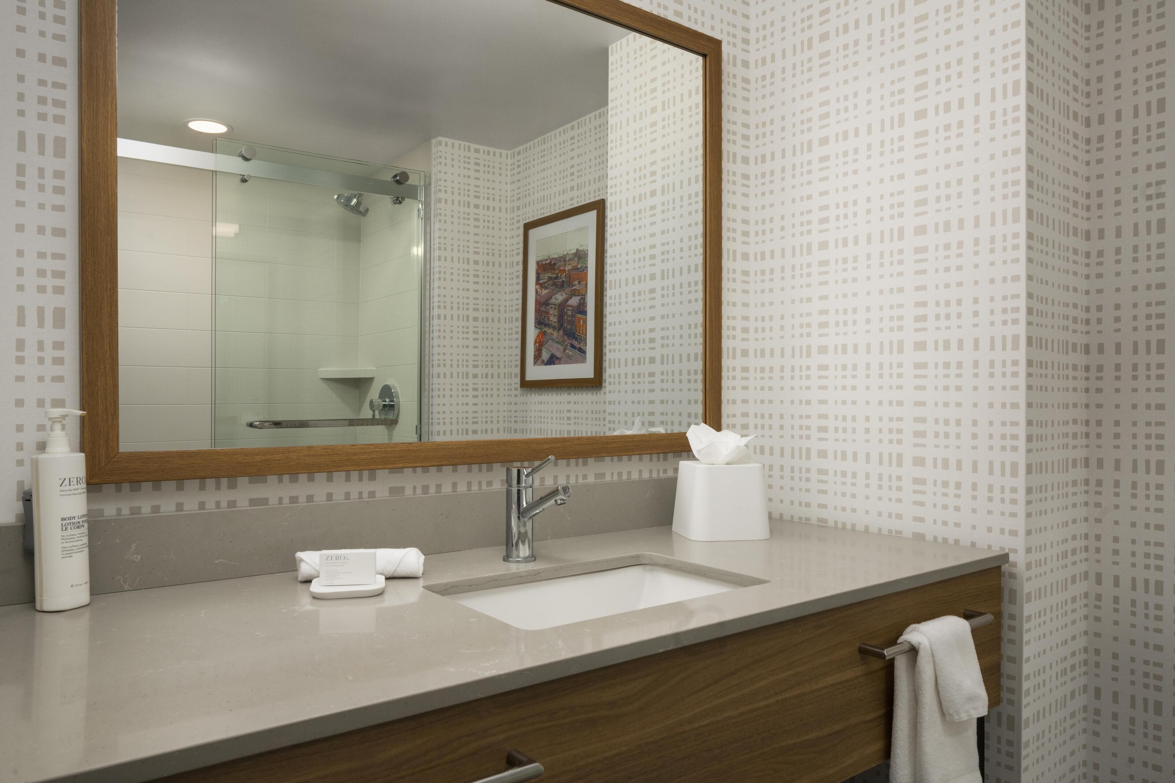 A bathroom with a large mirror, a sink, a towel rack, and a framed picture on the wall.