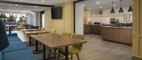 A modern dining area with tables and chairs, a kitchen area with appliances, and a large window with a view of trees.