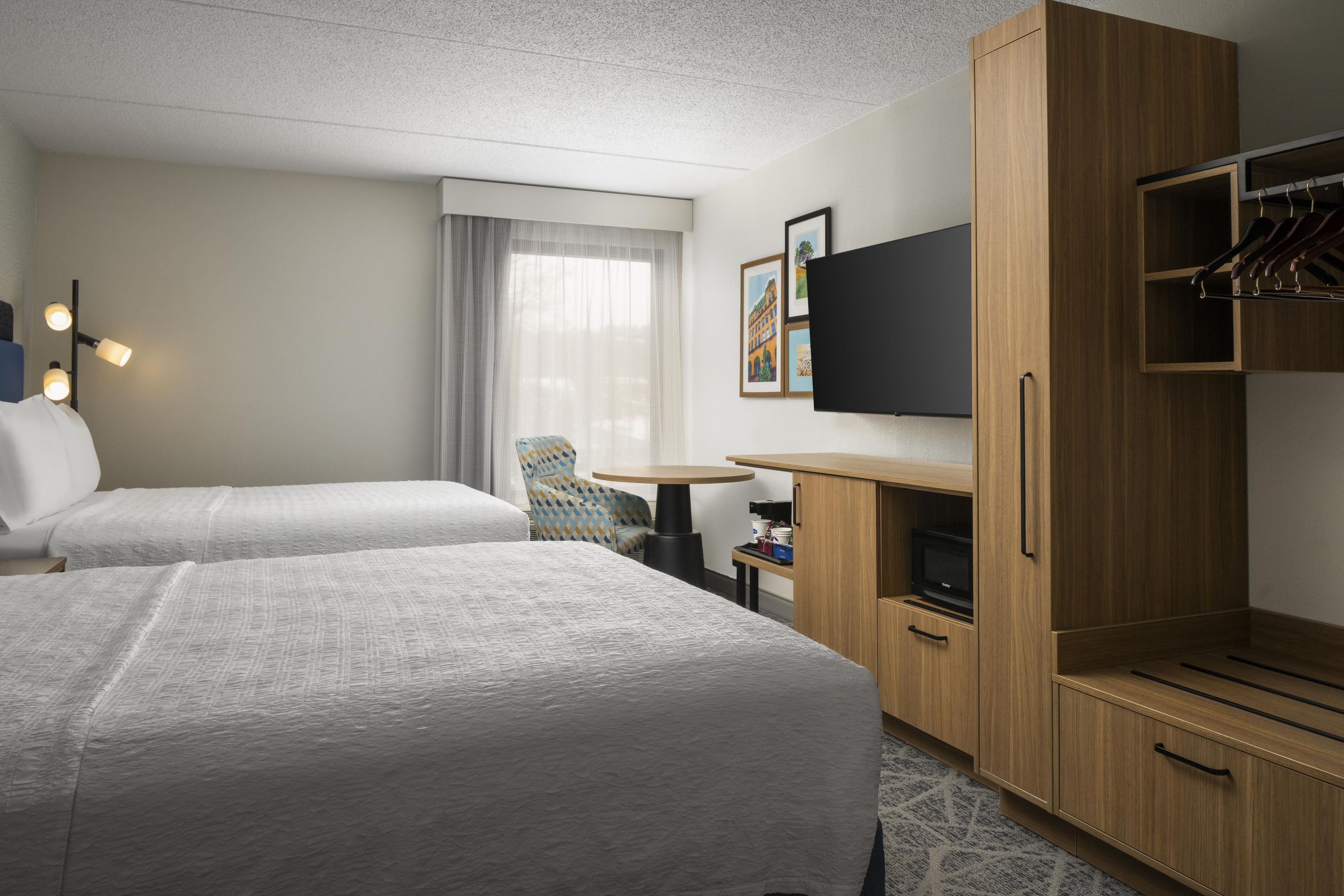 Una habitación de hotel con dos camas, un escritorio, una silla, un televisor y un armario.