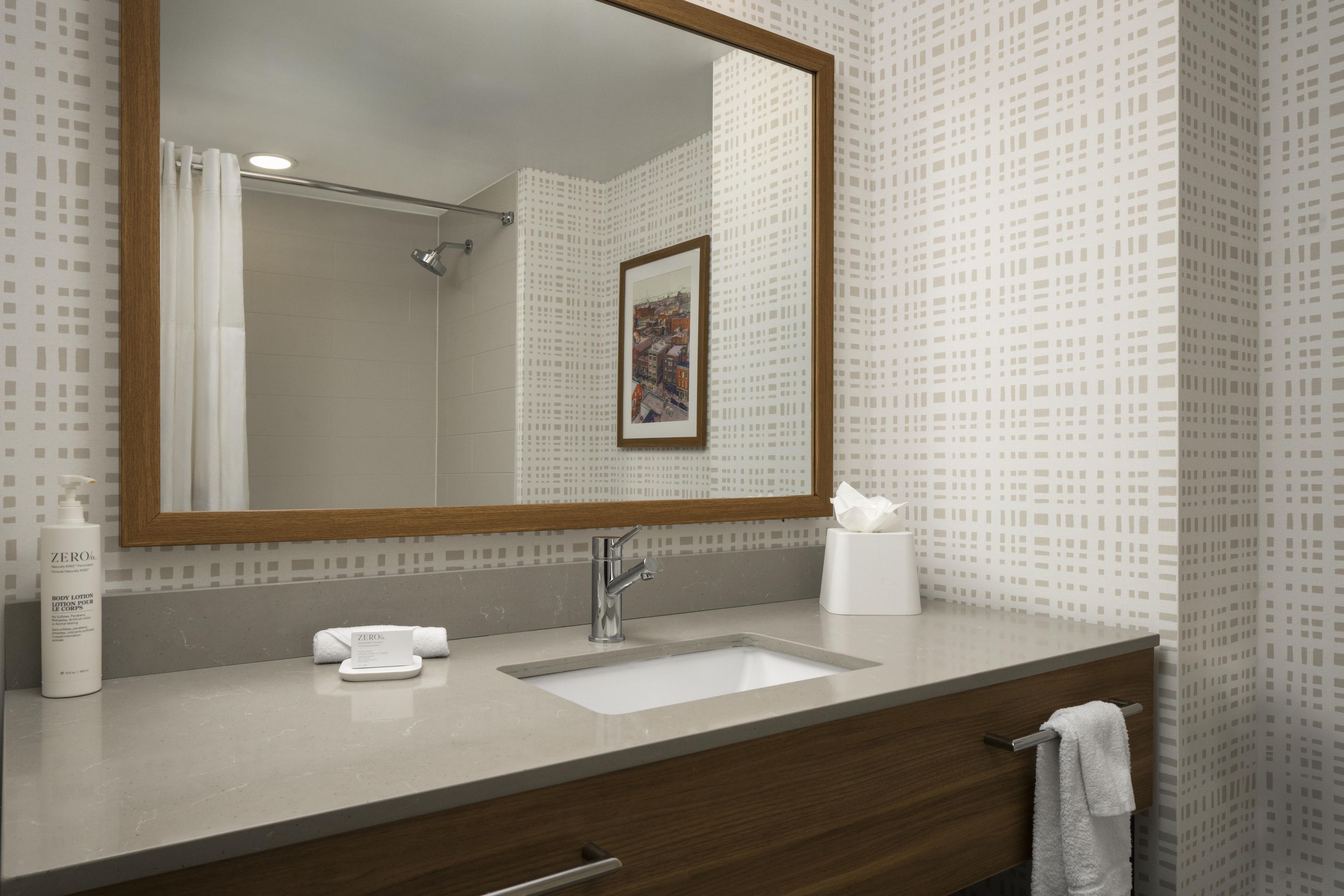 Une salle de bain avec un grand miroir, un lavabo, une serviette et un flacon de lotion.
