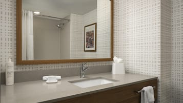Une salle de bain avec un grand miroir, un lavabo, une serviette et un flacon de lotion.