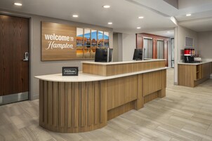 Una recepción con un cartel que dice 'Welcome to Hampton', una estación de café y vistas de un edificio a través de una ventana.