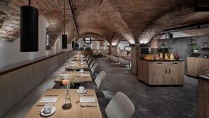 A restaurant with brick arches, wooden tables, and a kitchen area. - Hotel Schwarzer Adler (Innsbruck)