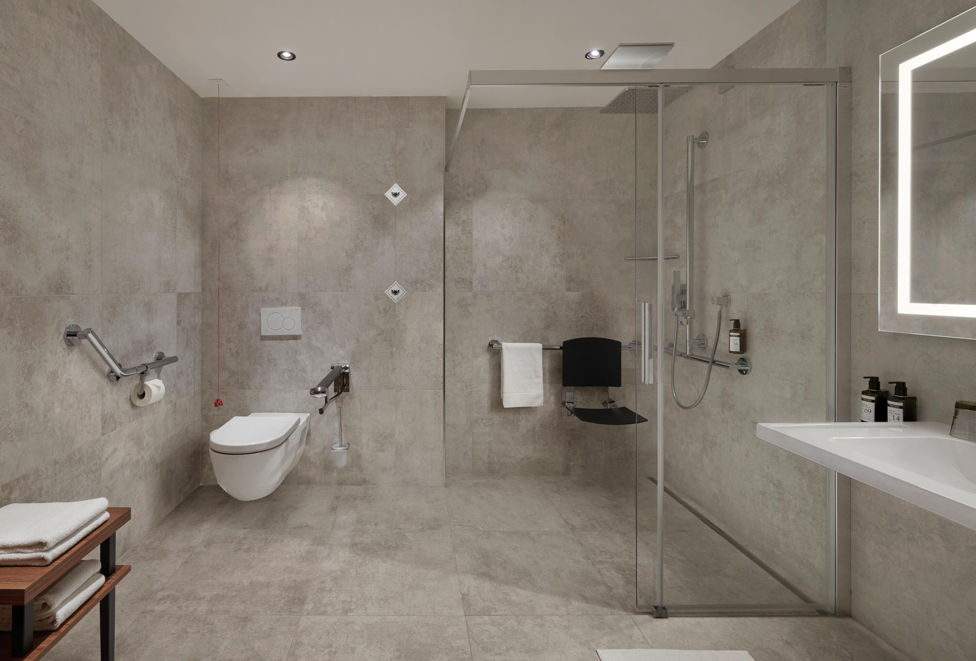 A modern bathroom with a glass-enclosed shower, a white sink, and a toilet with a grab bar.