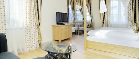 Una habitación de hotel con una cama, televisión, una mesita de centro de cristal y cortinas.